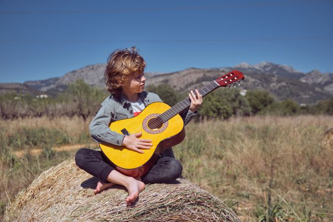 Boy playing guitar on hay roll