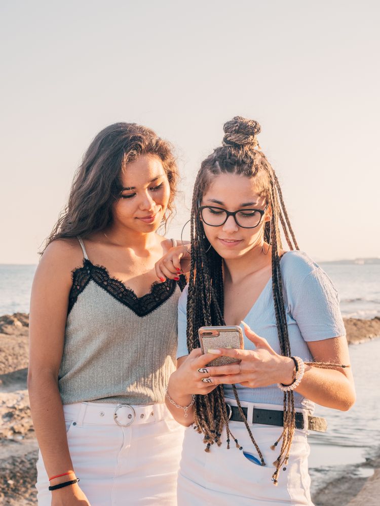 Smiling trendy young women using smartphone on beach