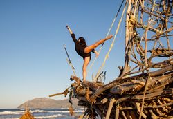 Young woman with upped leg on decorative wooden ship near water on shore