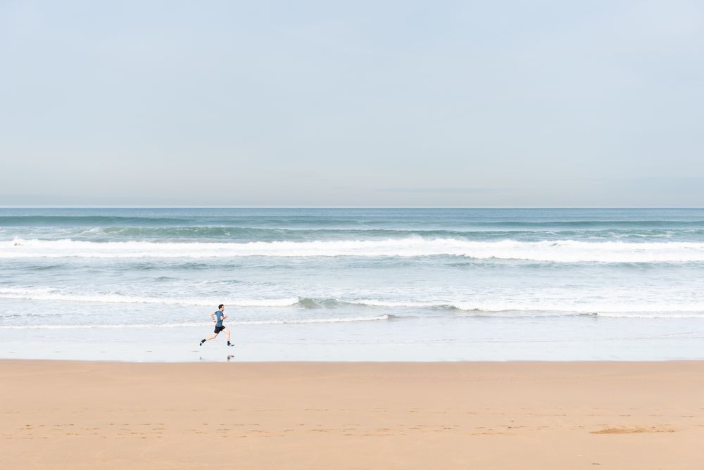 Sportsman in active wear jogging on lonely beach