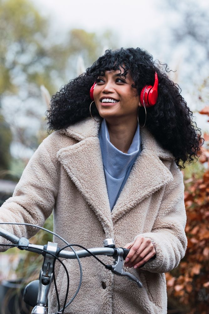 Cheerful Black woman in headphones with bicycle
