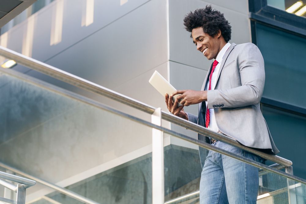 Happy man looking at his digital tablet while walking up staircase