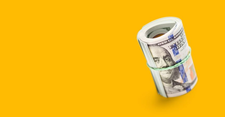 Roll Of One Hundred Dollar Bills Secured with a Rubber Band on a Yellow Ochre Background.