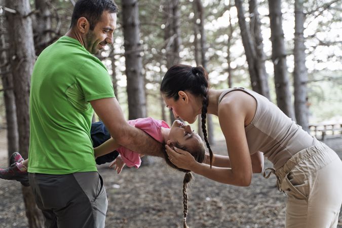 Mother kissing daughter playing sleeping beauty in forest with father