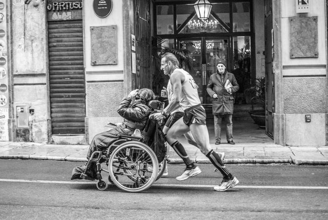 Side view of man running the marathon with a person on wheel chair in grayscale