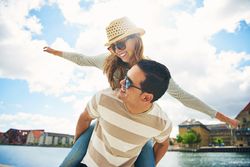 Joyful couple having fun near the river with man giving woman piggy back