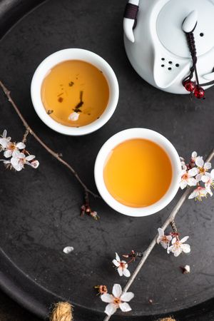 Top view of teapot and two cups on tray with floral garnish