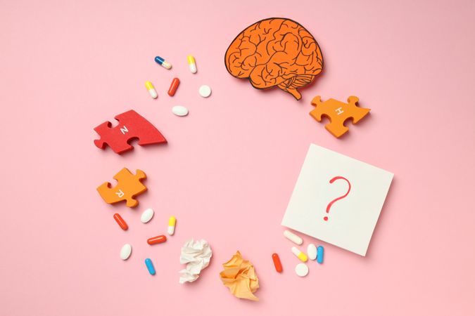 Pink paper with circle of pills, puzzle pieces, brain and question mark with copy space