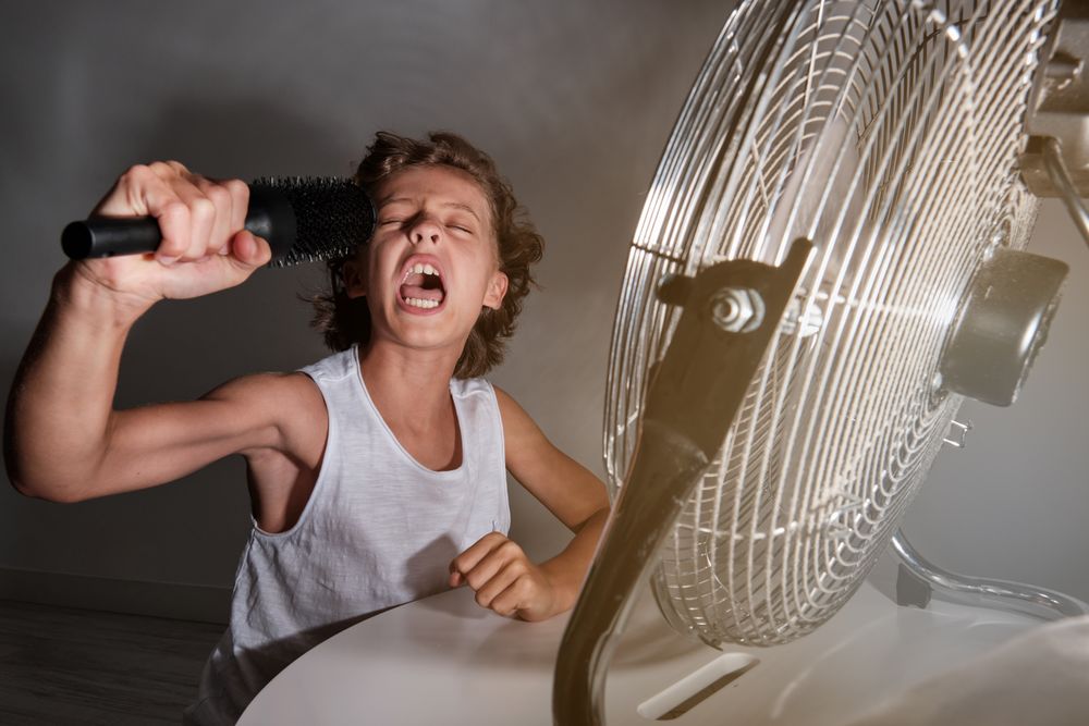 Excited preteen boy shouting into comb in front of working fan