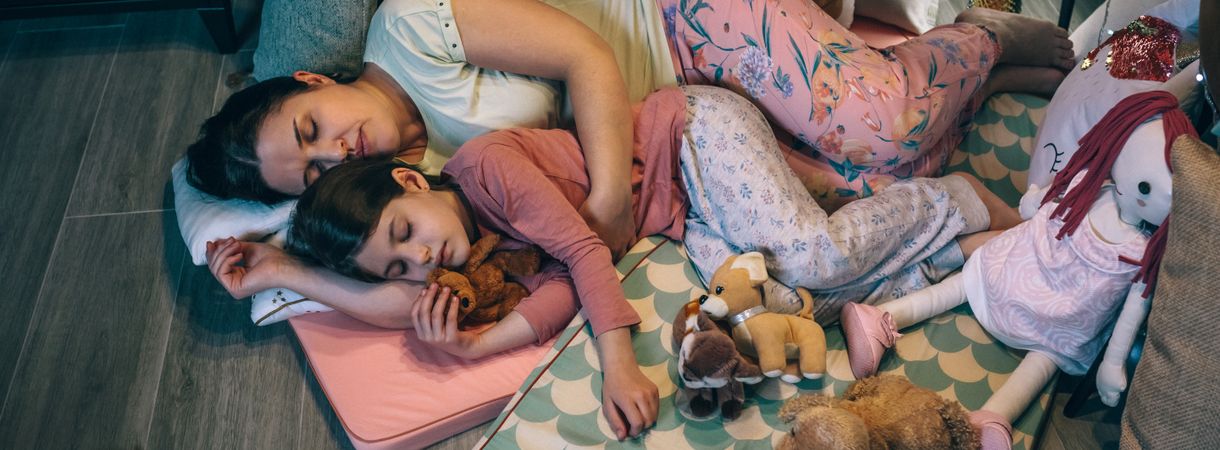 Banner of mother embracing to daughter with closed eyes asleep surrounded by cushions at night.
