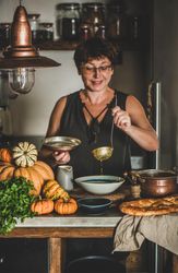 Woman with short hair and glasses with soup ladle in kitchen in cozy kitchen