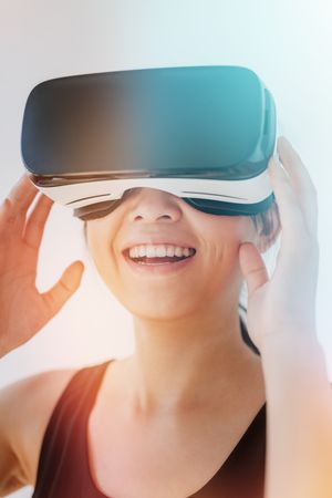 Close up shot of smiling young woman using the virtual reality headset against grey background