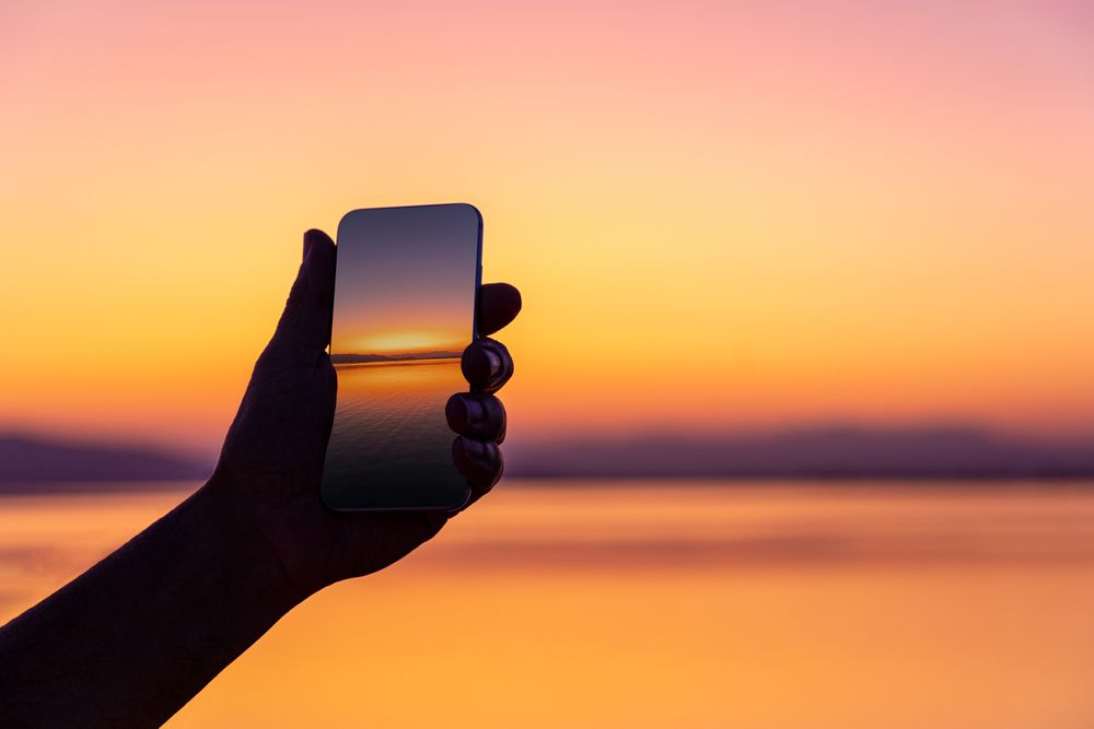 Crop traveler with photo of sunset on smartphone