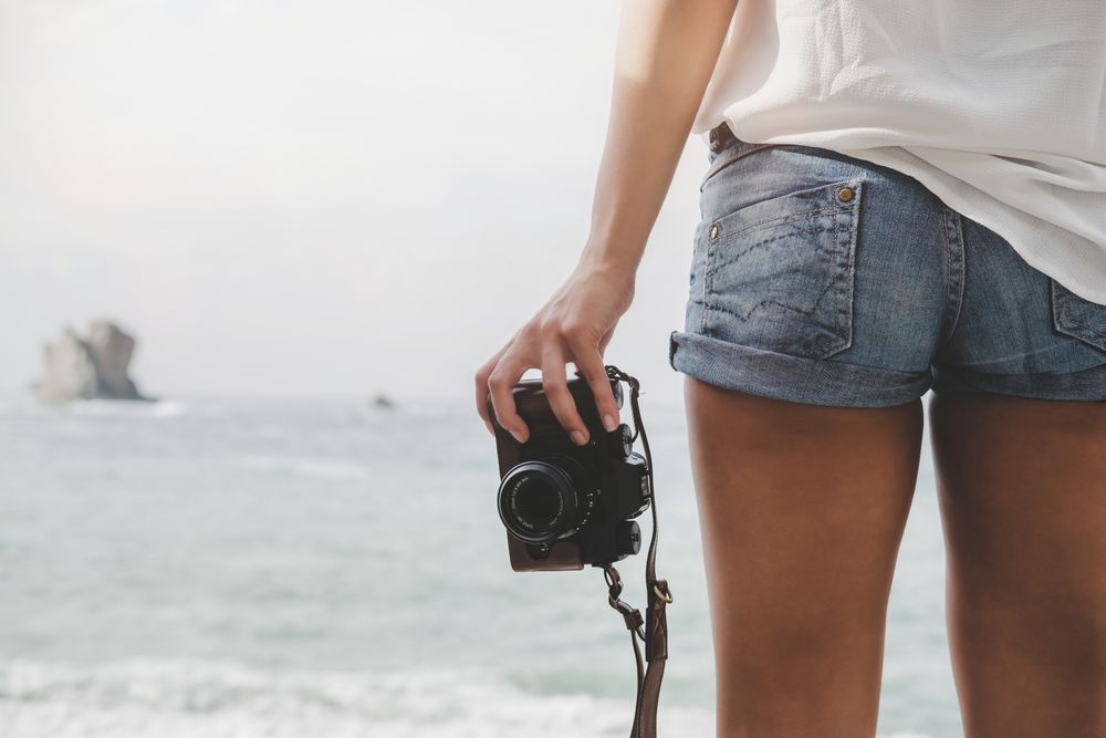 Woman with camera on shore near stones and water