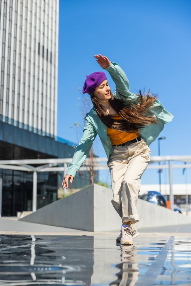 Energetic Young Woman Dancing Outdoors In Urban Setting, Wearing A Purple Beret And Stylish Spring Outfit