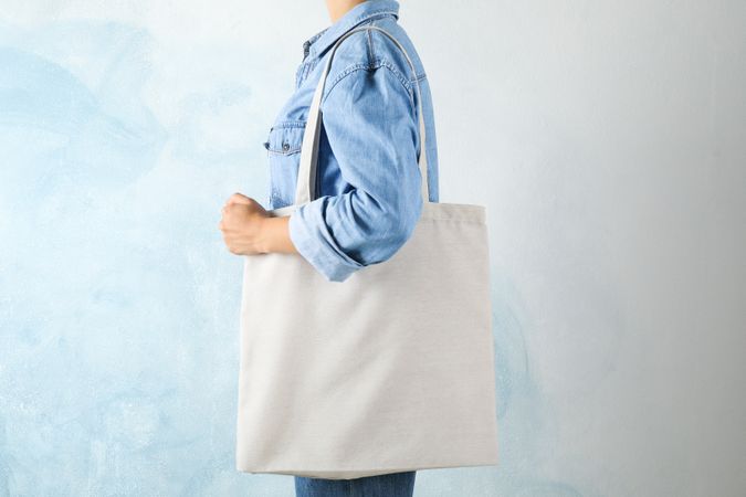 Young woman holding tote bag against blue background, empty space
