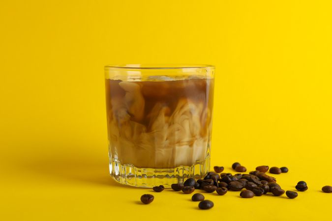 Glass of ice coffee on yellow background. Fresh drink