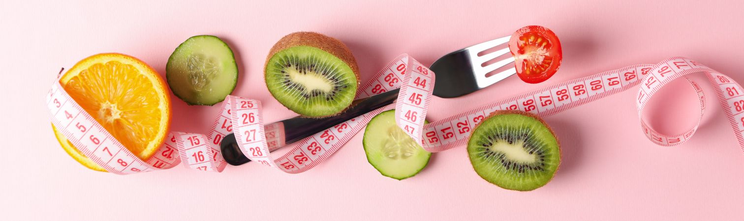 Fork, measuring tape and vegetarian food on pink background