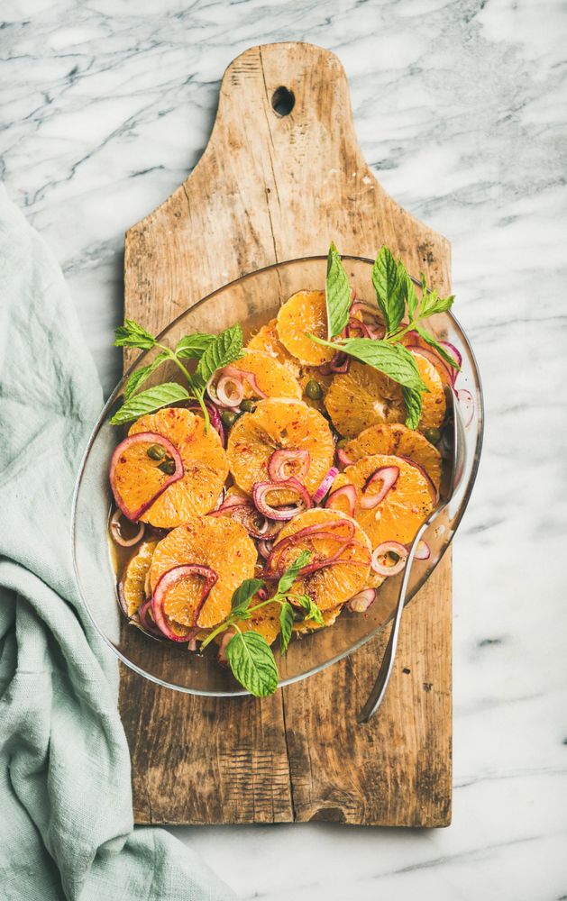 Mediterranean orange dish with onions, mint, and silver serving spoon on wooden board