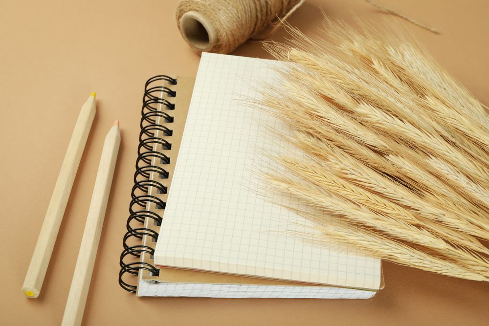 Close up of notebook with dried flowers, yarn, pencils on neutral brown background