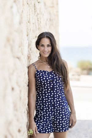 Latina woman in blue dotted dress leaning on wall outside
