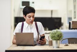 Woman in loft apartment checking her smart phone while working at home