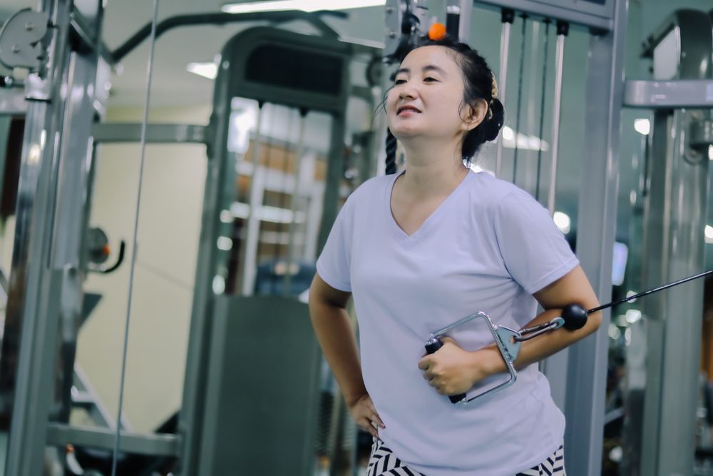 A woman asia uses a cable machine at a gym