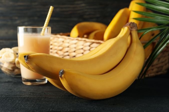 Bananas, juice and palm branch on wooden background. Fresh fruit