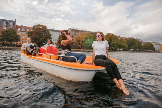 Outdoors shot of young friends relaxing on pedal boat on river in the city