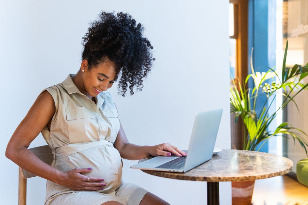 Smiling Black woman touching belly while browsing laptop
