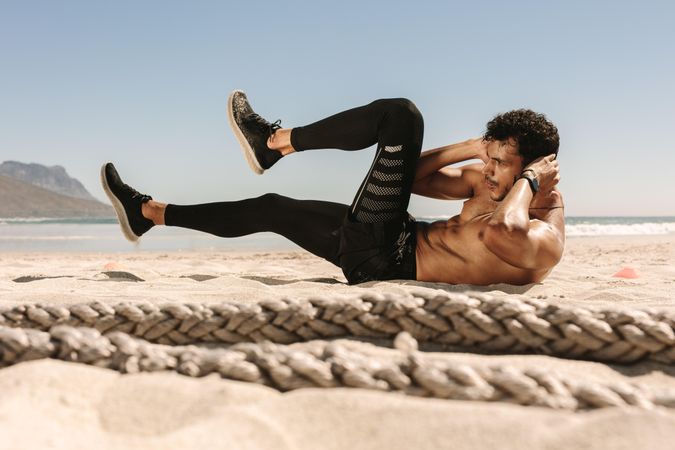 Side view of fit man doing abdomen workout on a beach