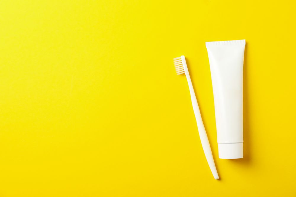 Toothbrush and toothpaste on yellow background, space for text