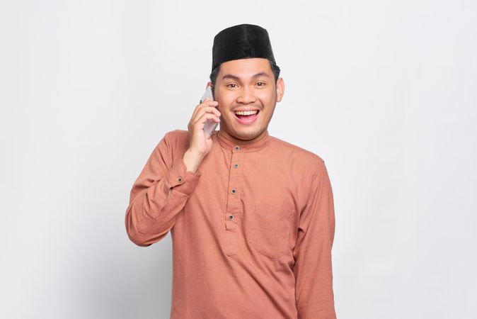 Muslim man in kufi hat smiling and talking on smartphone