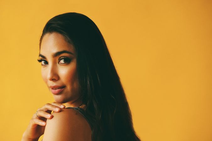 Elegant Hispanic woman looking around at camera in yellow room with her hand on her shoulder