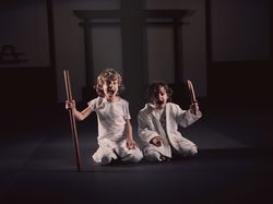 Funny kids in judogi sitting on mat with wooden sticks and shouting