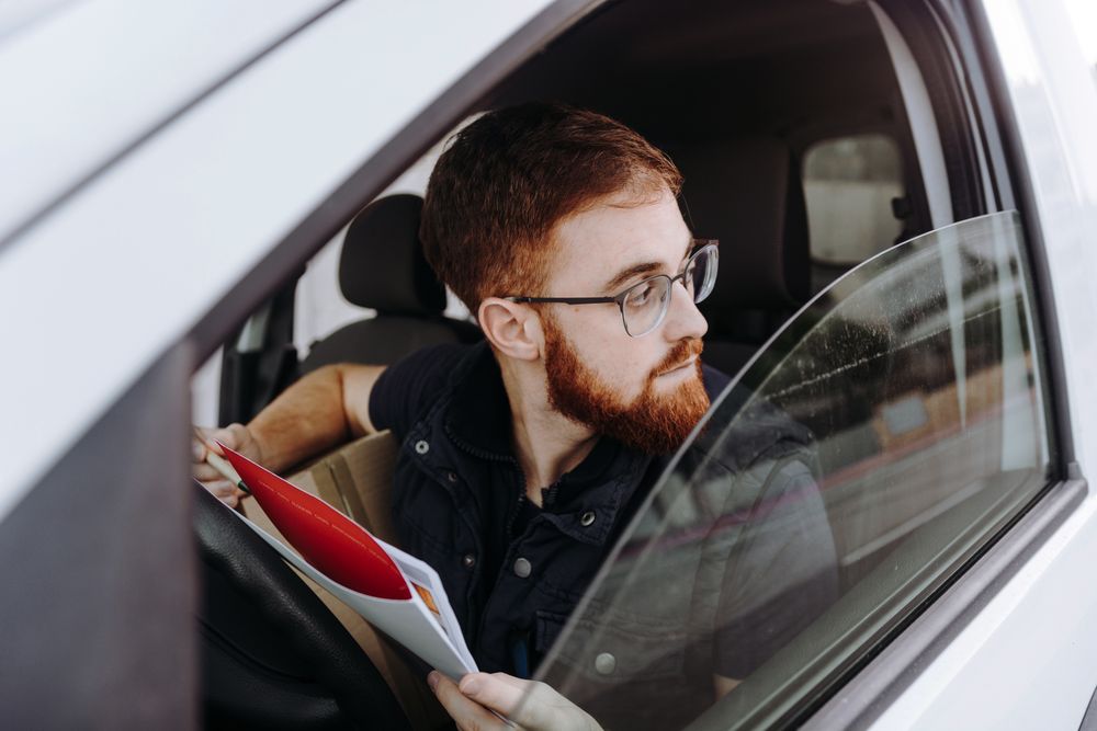 Courier filling papers while preparing for delivery of order to client in car