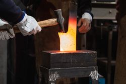 Blacksmiths forging hot metal with hammer in workshop