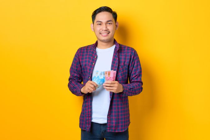 Smiling Asian man in plaid shirt holding banknotes