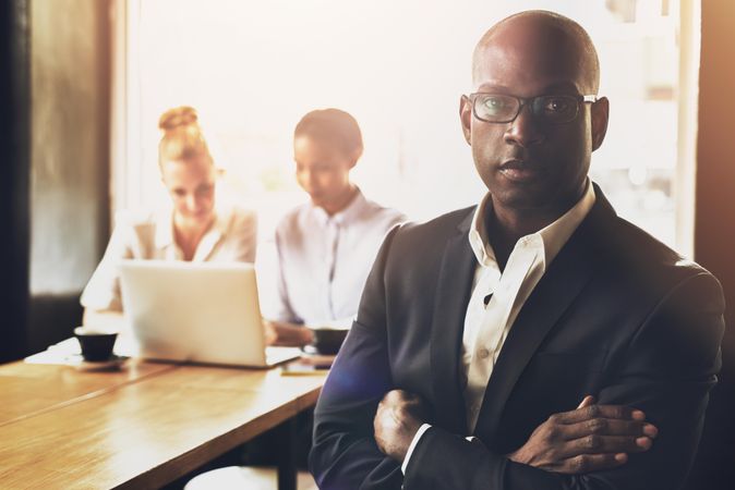 Black businessman pictured with his arms crossed in front of his colleagues