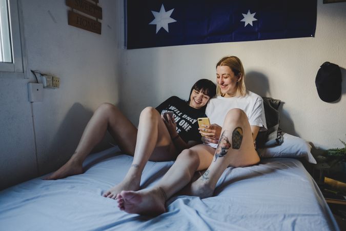 Happy lesbian couple using smartphone on bed