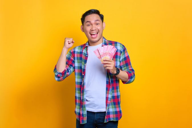 Smiling happy Asian man holding money he won in studio shoot