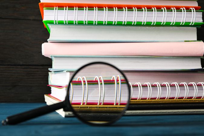 Composition with copybooks and magnifier on wood table against dark background