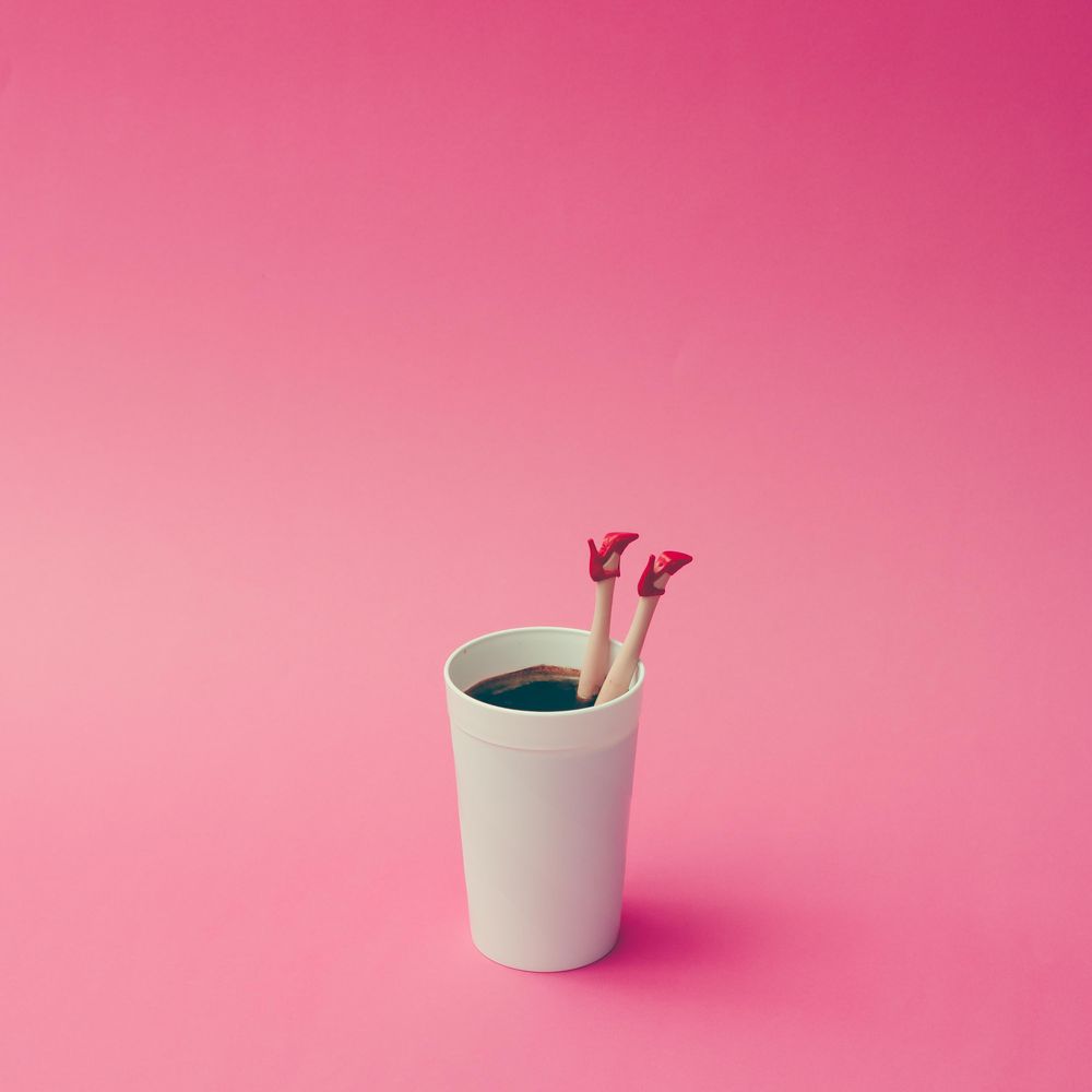 Coffee cup with female doll legs on pink background, with copy space