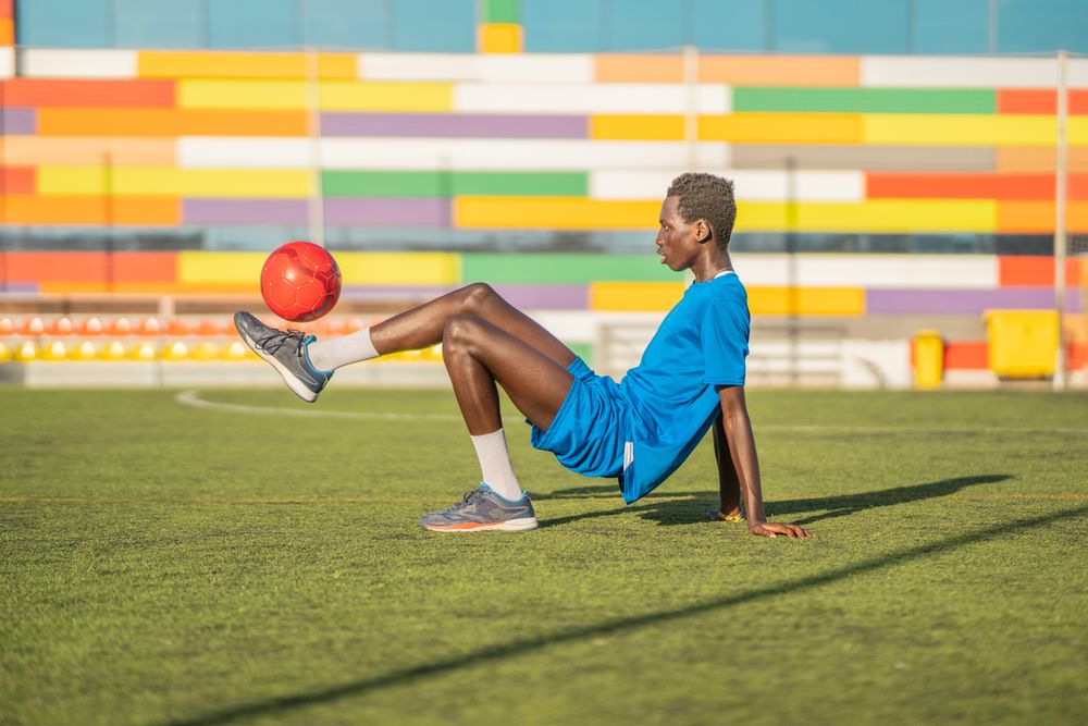 Black teenager bouncing football ball on foot