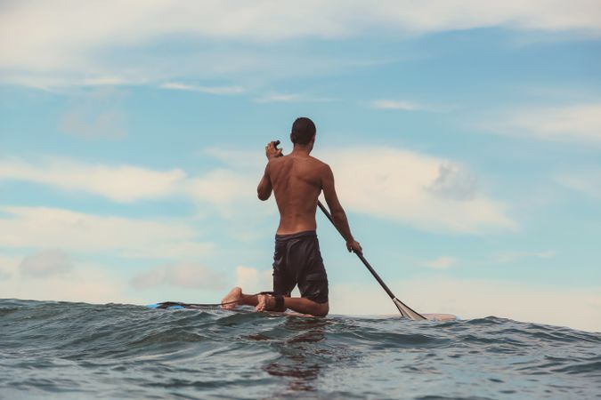 Man with paddle on surf board waving on water