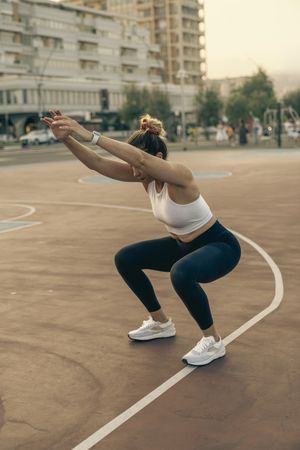 Fit woman demonstrating the proper form for a squat exercise in an urban park