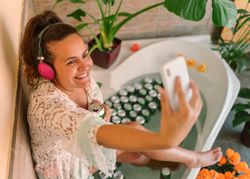 Cheerful woman in bathtub taking selfie