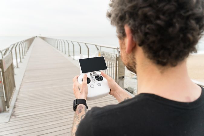 Rearview man with remote for drone on wooden boardwalk on beach