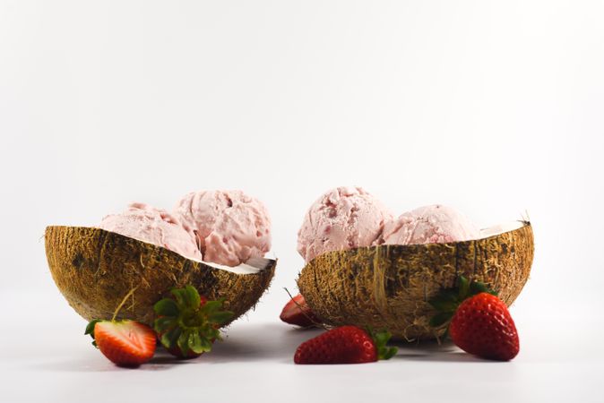 Side view of two coconut shells with delicious ice cream and strawberry fruit