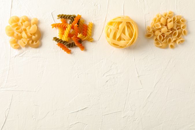 Flat lay composition with different pasta on light background, space for text. Dry uncooked whole pasta